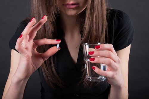 Xanax Addiction: What You Need to Know - brunette girl about to take blue pill with water