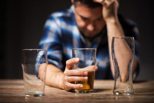 upset man drinking beer from glass with two empty glasses on bar - alcohol use disorder