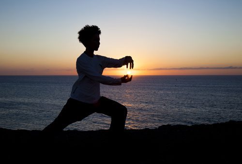 silhouette of person doing tai-chi at sunset or sunrise - meditation
