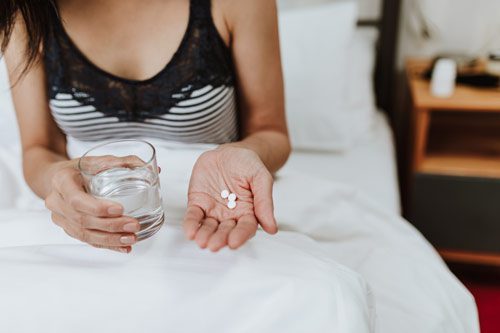 cropped image of woman sitting up in bed about to take 3 little white pills with a glass of water - Ambien