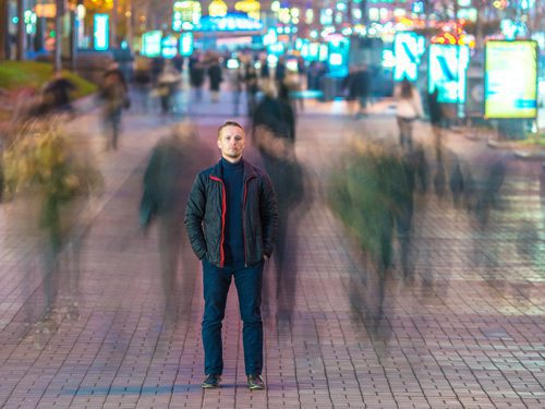 man standing in focus on busy street where others in crowd are blurred - risk factors for addiction