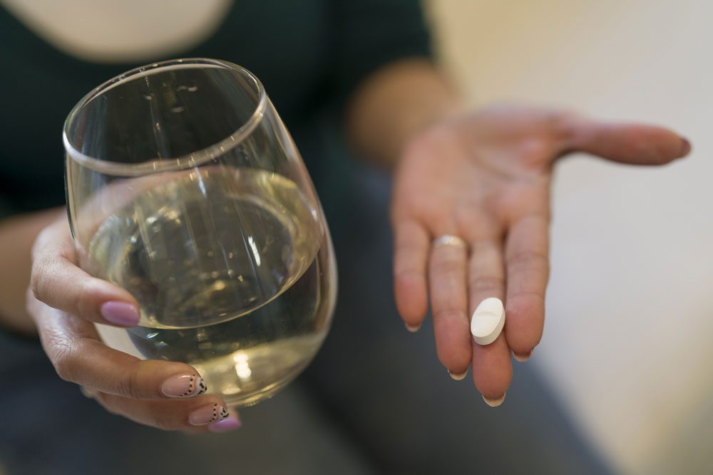 Woman holding a glass of wine in one hand and a pill in the other - dangers of mixing alcohol and drugs