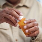 Close-up of a person’s hands opening an orange prescription pill bottle, symbolizing opioid use or medication management.