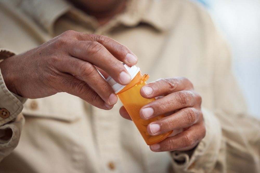 Close-up of a person’s hands opening an orange prescription pill bottle, symbolizing opioid use or medication management.