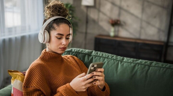 Excited young woman listening to music on wireless headphones over a mobile app while sitting on a comfortable sofa
