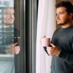Man holding coffee or tea looking contently out the window