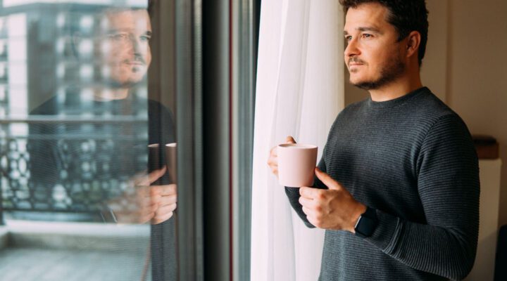 Man holding coffee or tea looking contently out the window