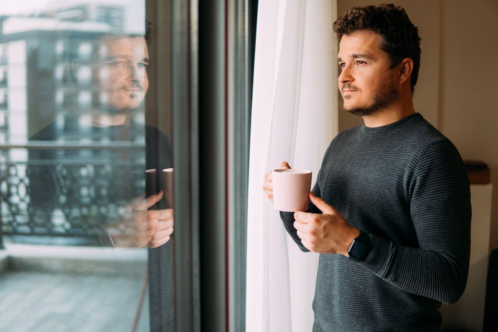 Man holding coffee or tea looking contently out the window