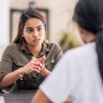 Woman speaking with a healthcare professional during a counseling session, appearing serious and engaged in conversation.