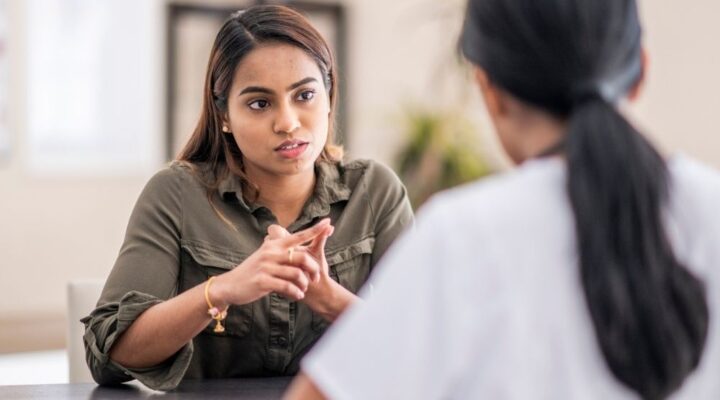 Woman speaking with a healthcare professional during a counseling session, appearing serious and engaged in conversation.