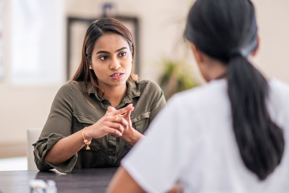 Woman speaking with a healthcare professional during a counseling session, appearing serious and engaged in conversation.